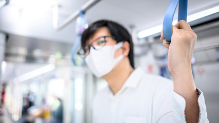 Fototapeta na wymiar Asian man wearing surgical face mask holding handrail on skytrain or urban train. Wuhan coronavirus (COVID-19) outbreak prevention in public transportation. Health awareness for pandemic protection