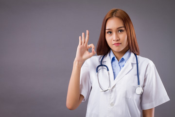 portrait of smiling asian woman doctor isolated, confident and friendly female doctor pointing ok or okay hand sign for approval, good, yes, acceptance