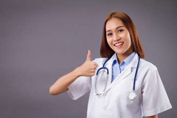 portrait of smiling asian woman doctor isolated, confident and friendly female doctor pointing thumb up hand sign for approval, good, yes, ok