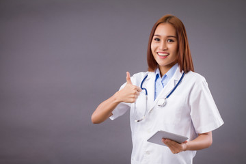 asian woman doctor giving thumb up and using smart computer tablet in job; concept of medication with technology, AI in hospital, high technology doctor