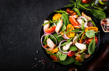 Spring salad with spinach, grilled chicken, cherry tomatoes, arugula, corn salad and red onion. Healthy food concept. Black stone table. Top view. Copy space