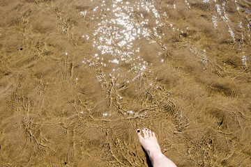 The girl's foot comes on the sand covered with a transparent layer of water that glitters in the sun