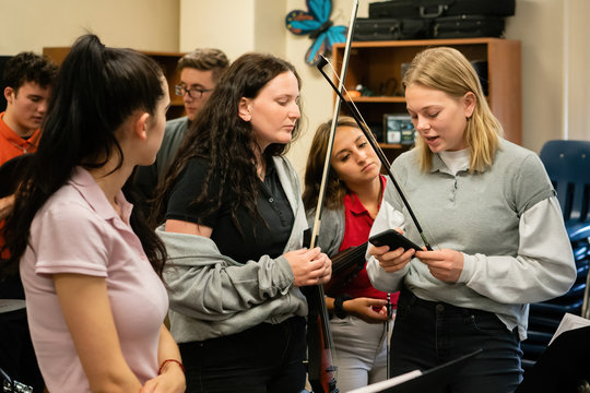 Group of high school musicians consulting a mobile device during music rehearsal