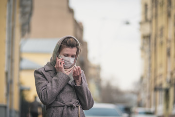 Fototapeta premium Young woman in a protective mask talking on a smartphone on the street