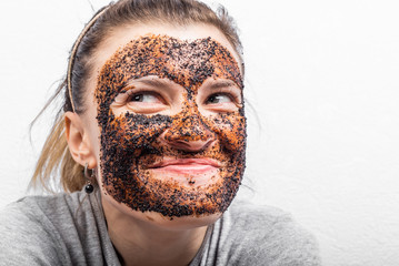 Smiling young attractive woman with scrub on her face - coffee cleansing scrub