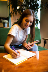 Young woman writes in her planner and holds mobile phone working freelance place