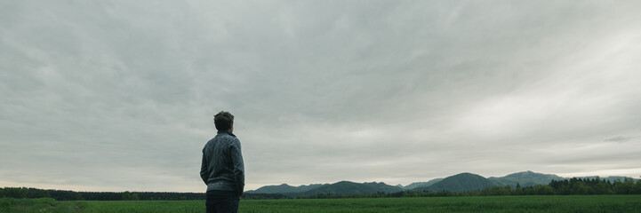Young man standing under grey cloudy sky