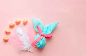 Egg gift in green paper packaging and with pink ribbon Easter Bunny wrap idea. Chocolate dragee white and gold color, multicolor colorful feathers. Minimal concept. Flat lay, Copy space, top view