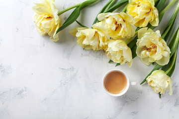 Morning coffee and beautiful bunch of tulip flowers on white stone table top view. Flat lay style. Cozy breakfast on Mother or Woman day.