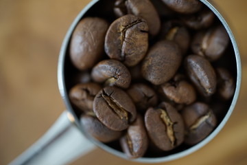 Kaffeebohnen in einem Kaffeedosierlöffel auf einem Holzbrett