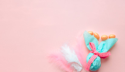 Egg gift in green paper packaging and with pink ribbon Easter Bunny wrap idea. Chocolate dragee white and gold color, multicolor colorful feathers. Minimal concept. Flat lay, Copy space, top view