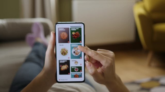 Orders Pizza Using Online Delivery. Woman Orders Food Home In Online Store Using a Smartphone. Female Ordering pizza using food delivery app. Screen is blurred. Focus on hand.