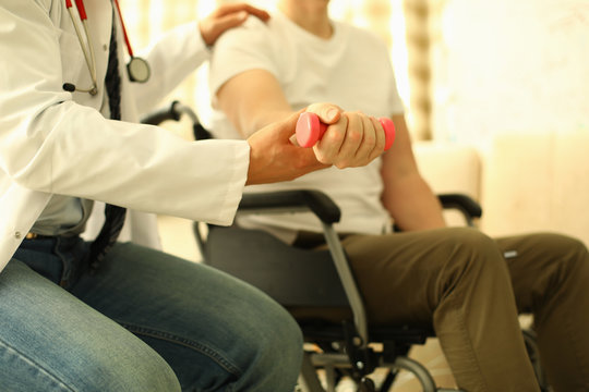 Handicapped man sits working out dumbbell arm. Rehabilitation after injuries. Treatment and restoration lost functions. Restoration motor functions hand. Restore and adapt to life after an accident
