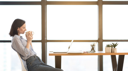 Young woman using laptop and drinking hot tea