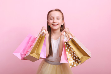 Beautiful smiling little girl with bags for shopping on a colored background. The concept of...