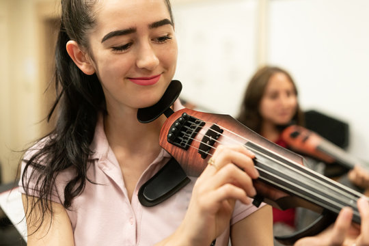 Female high school students playing electonic violins in music classroom during rehearsal