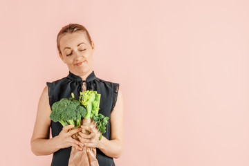 Healthy lifestyle. Girl holds broccoli and green vegetables in her hands, pink background. Diet and...