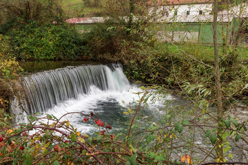waterfall in an autumnal landscape near a villa with leafy trees