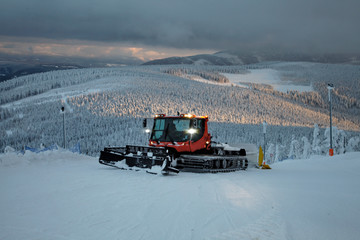 Czerwony ratrak śnieżny na stoku narciarskim zimowe panoramy Sudetów o zmierzchu Czarna Góra Polska