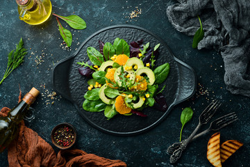 Obraz na płótnie Canvas Fresh vegan avocado salad with oranges and spinach on a black plate. Rustic style. Top view. Free space for your text.