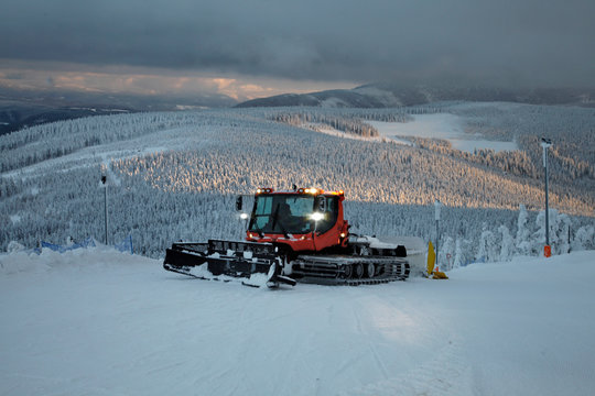 Czerwony ratrak śnieżny na stoku narciarskim zimowe panoramy Sudet&oacute;w o zmierzchu Czarna G&oacute;ra Polska