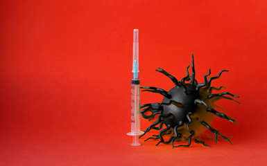 A black bulk virus molecule and a syringe with a needle on a red background. Selective focus. Vaccination. Protection against ncov 2019 coronavirus