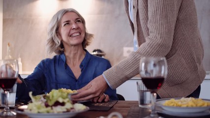 Slow motion shot of mature man serving dinner to his wife in kitchen