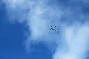 A seaside nautical search and rescue helicopter with rotating blades in the distance with a vivid bright blue sky and clouds. Rescue helicopter and rescue teams are brave.
