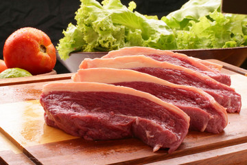 bife de picanha fatiado na tábua de churrasco, tomates e alfece ao fundo, fundo escuro