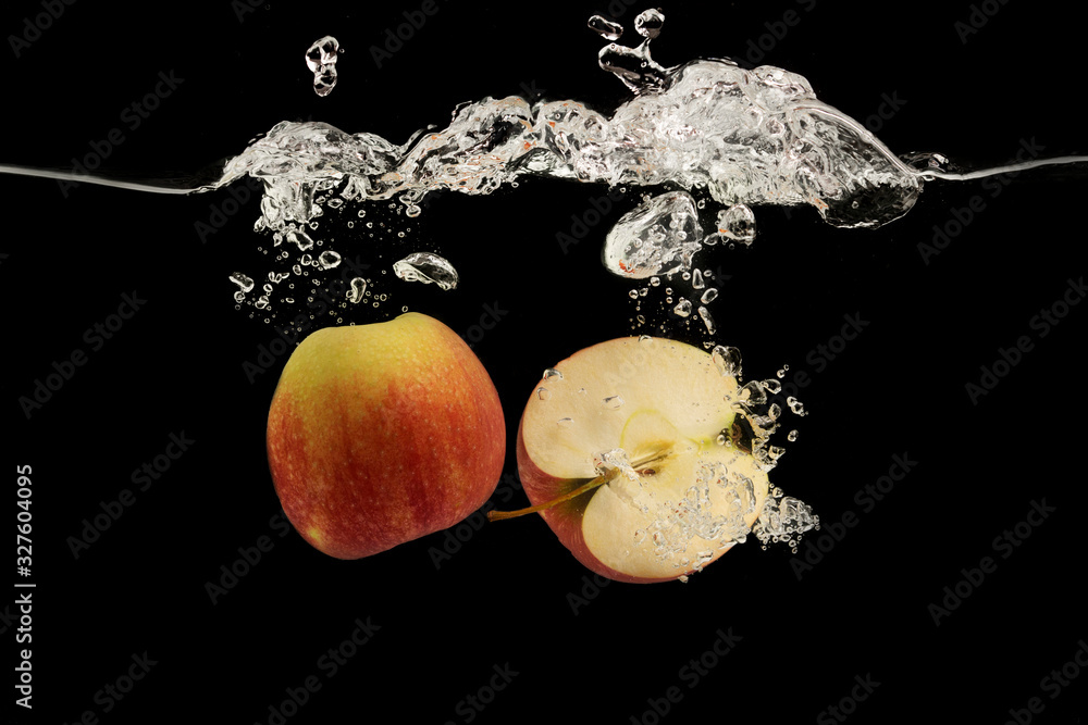 Poster halves of red apple flowing into clear water with splash on black background