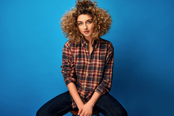 Portrait of young woman with blonde curly hair wear cotton check shirt isolated on blue background