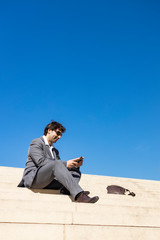 Smiling young business man sitting on steps with a cellphone