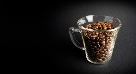 Glass with coffee beans on black background