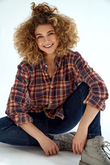 Fototapeta premium Young smiling woman with blonde curly hair wear cotton check shirt and sitting on white background