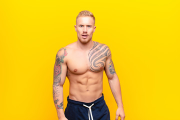 young strong blonde man feeling puzzled and confused, with a dumb, stunned expression looking at...