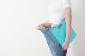 girl with scale pulling her big jeans and showing weight loss