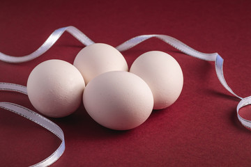 White eggs with fabric ribbon on red paper background, angle view, selective focus, happy Easter day