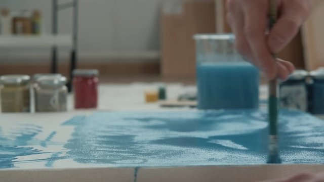 Unknown artist paints on a canvas, using a blue paint, close-up