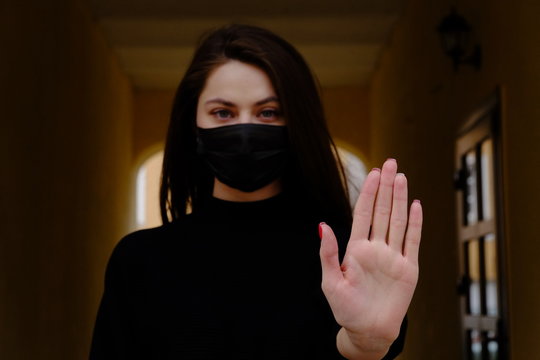 Girl, Young Woman In Protective Sterile Medical Mask On Her Face Looking At Camera Outdoors, On Asian Street Show Palm, Hand, Stop No Sign. Air Pollution, Virus, Chinese Pandemic Coronavirus Concept.