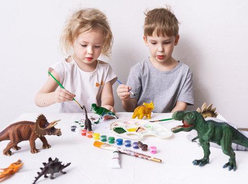 Children a boy and a girl are passionate and paint with figures and brush figures of toy dinosaurs.