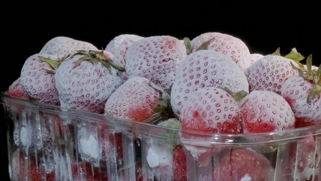 Fresh frozen strawberries in disposable plastic food pack on black background. Rotation 360 degrees, closeup