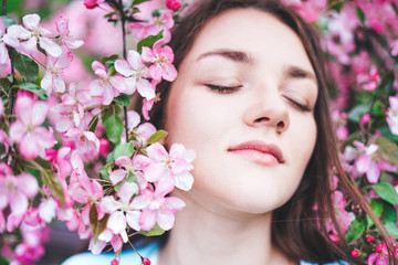 Fototapeta premium Young girl with closed eyes surrounded by flowers of a pink apple tree.