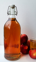 of a bottle and glass with natural apple juice. Apple cider drink of fermented fruit drink and organic apples on white. Homemade apple juice. Vertical composition