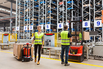 Storehouse employees in uniform standing near pallet truck and forklift in modern automatic warehouse.Boxes are on the shelves of the warehouse. Warehousing, machinery concept. Logistics in stock. © Алина Бузунова