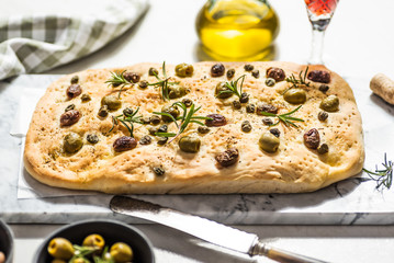 Foaccia with green and black olives, rosemary and capers. White background, hard light.