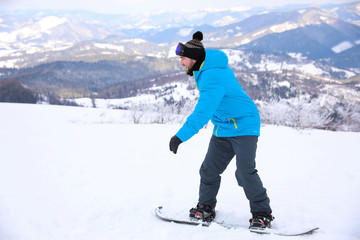 Fototapeta na wymiar Young man with snowboard on hill at mountain resort. Winter vacation
