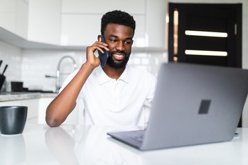 Young african man talk phone while use laptop in the kitchen