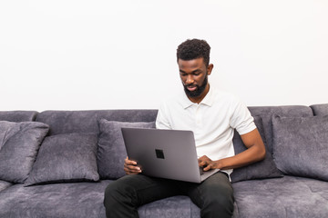 Handsome african american man sitting with laptop on sofa in room