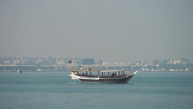 Retro historical boat with blurred panoramic view of modern skyline of Doha and green palms on background