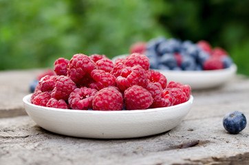 Still life with a blueberries and raspberries on an old wooden table, at the garden. Rural natural food style.